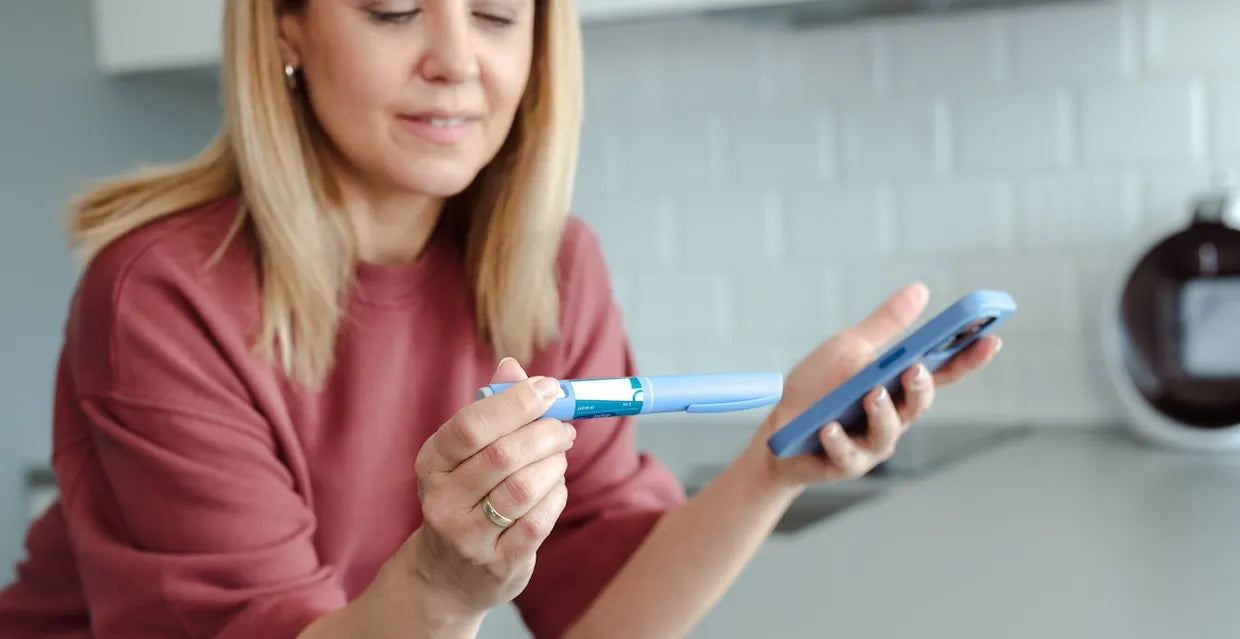 Woman preparing a semaglutide (GLP-1) injection pen while checking dosing on her phone at home